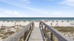A wooden boardwalk leading to a beach with red umbrellas and lounge chairs. - Ocean Breeze West 705 (Pensacola)