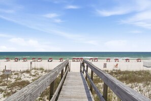 A wooden boardwalk leading to a beach with red umbrellas and lounge chairs. - Ocean Breeze West 705 (Pensacola)