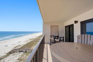 A balcony with a view of the beach, a table, and two chairs. - Ocean Breeze West 705 (Pensacola)