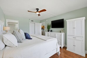 A bedroom with a bed, a ceiling fan, a television, and white cabinetry. - Ocean Breeze West 705 (Pensacola)