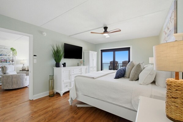 A bedroom with a bed, a television, a ceiling fan, a window with a view, and a white dresser. - Ocean Breeze West 705 (Pensacola)