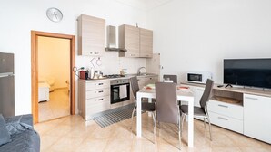 A modern kitchen with white cabinets, a stove, microwave, and a dining area with a table and chairs. - Casa Alessia by Rentbeat (Cisternino)