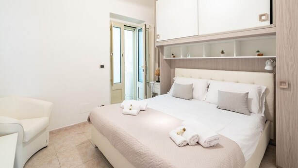 A bedroom with a bed, a chair, a wardrobe, and a door leading to a balcony. - Casa Alessia by Rentbeat (Cisternino)