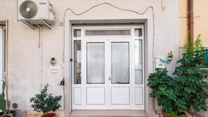 A building entrance with a white door, a small potted plant, and an air conditioning unit. - Casa Alessia by Rentbeat (Cisternino)
