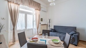 A dining area with a table set for two, a sofa, and a window with curtains. - Casa Alessia by Rentbeat (Cisternino)