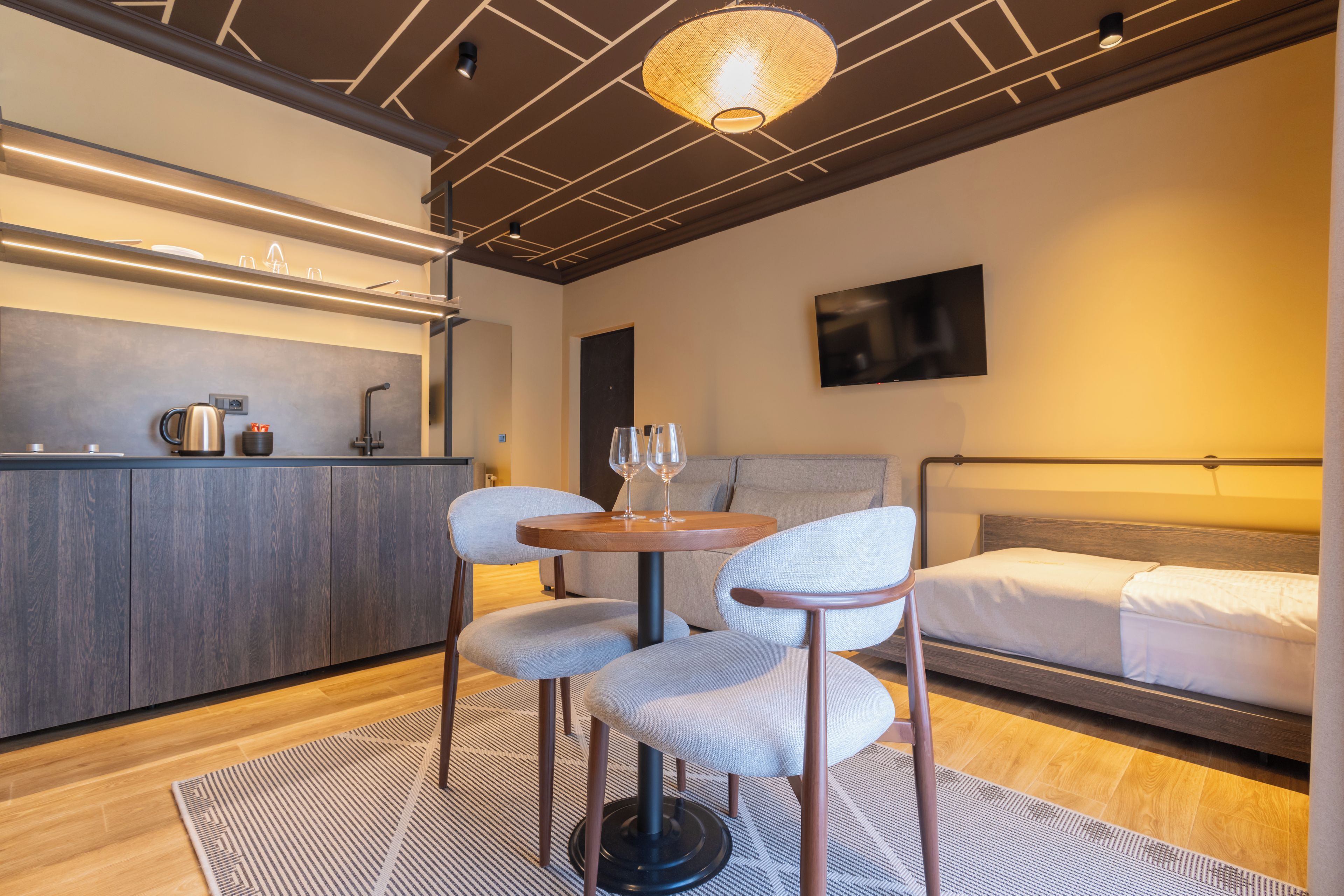 A modern hotel room with a kitchenette, a bed, and two chairs.