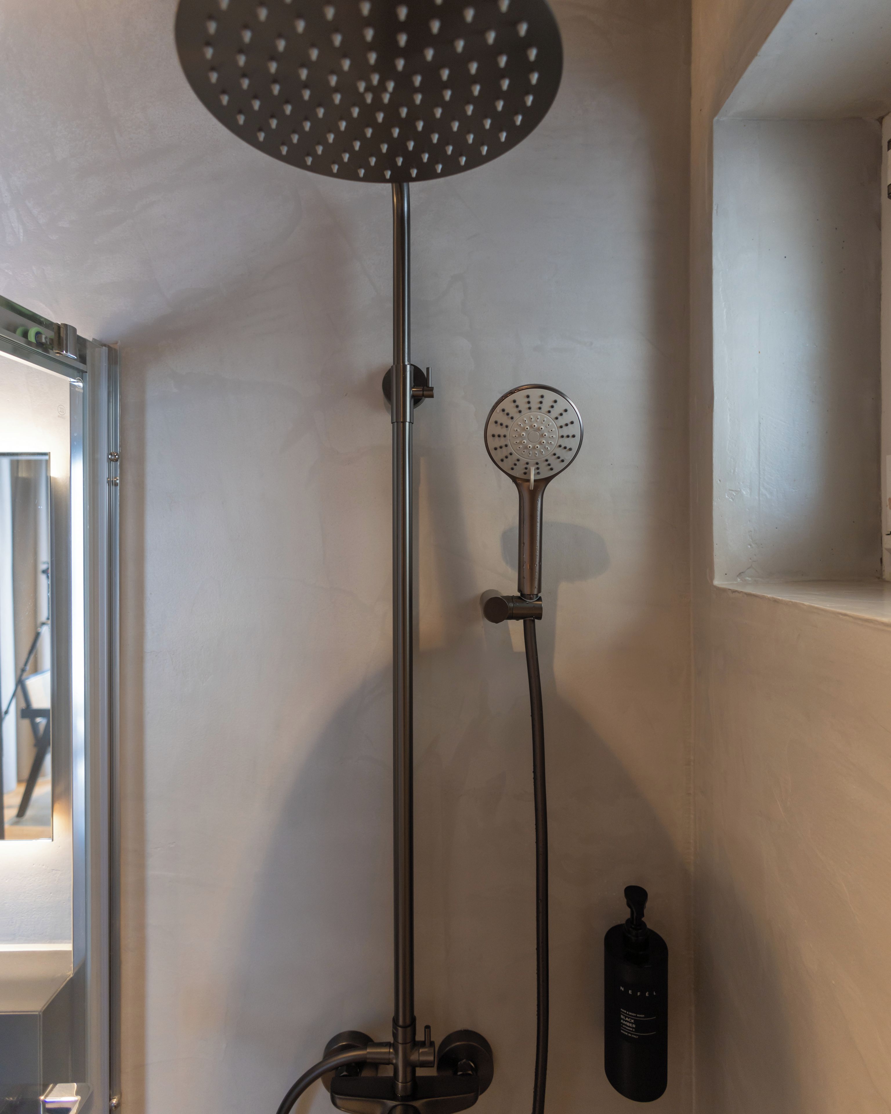 A shower with a circular head and a handheld showerhead attached to a vertical rod.