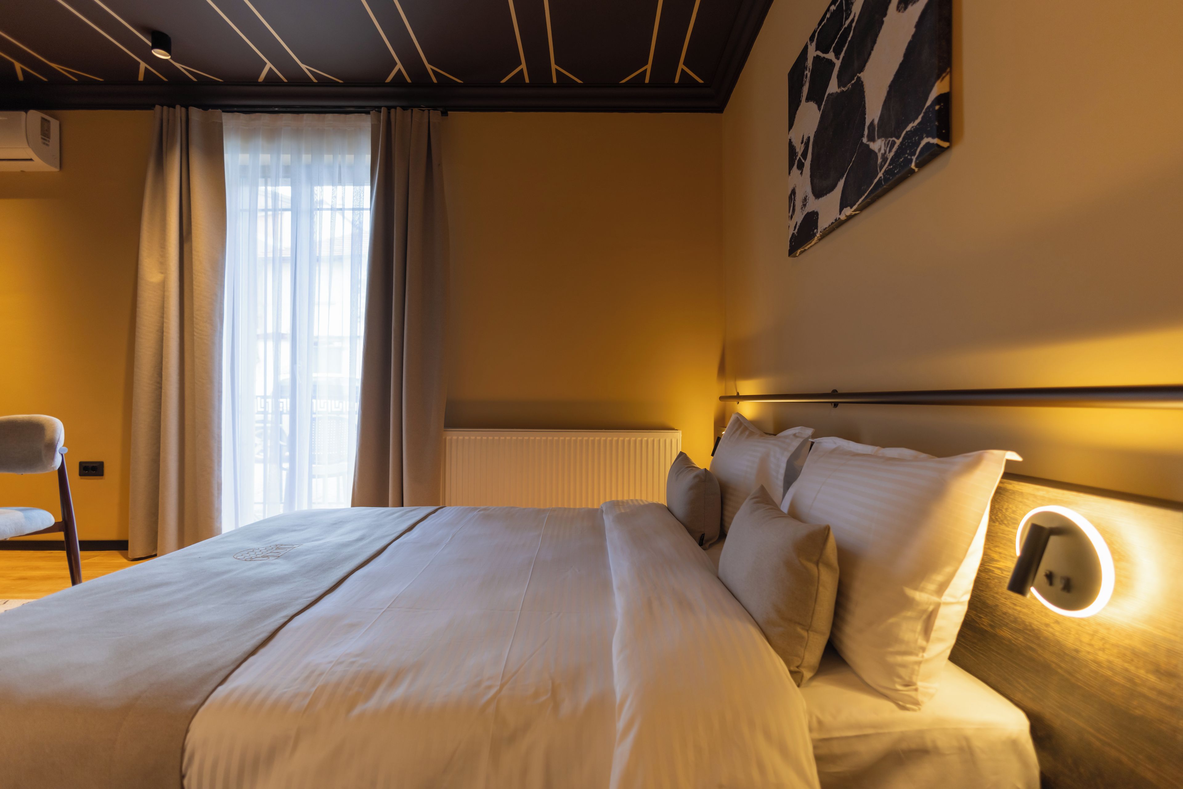 A hotel room with a large bed, a chair, a radiator, and a wall-mounted light fixture.