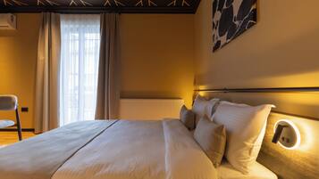 A hotel room with a large bed, a chair, a radiator, and a wall-mounted light fixture.