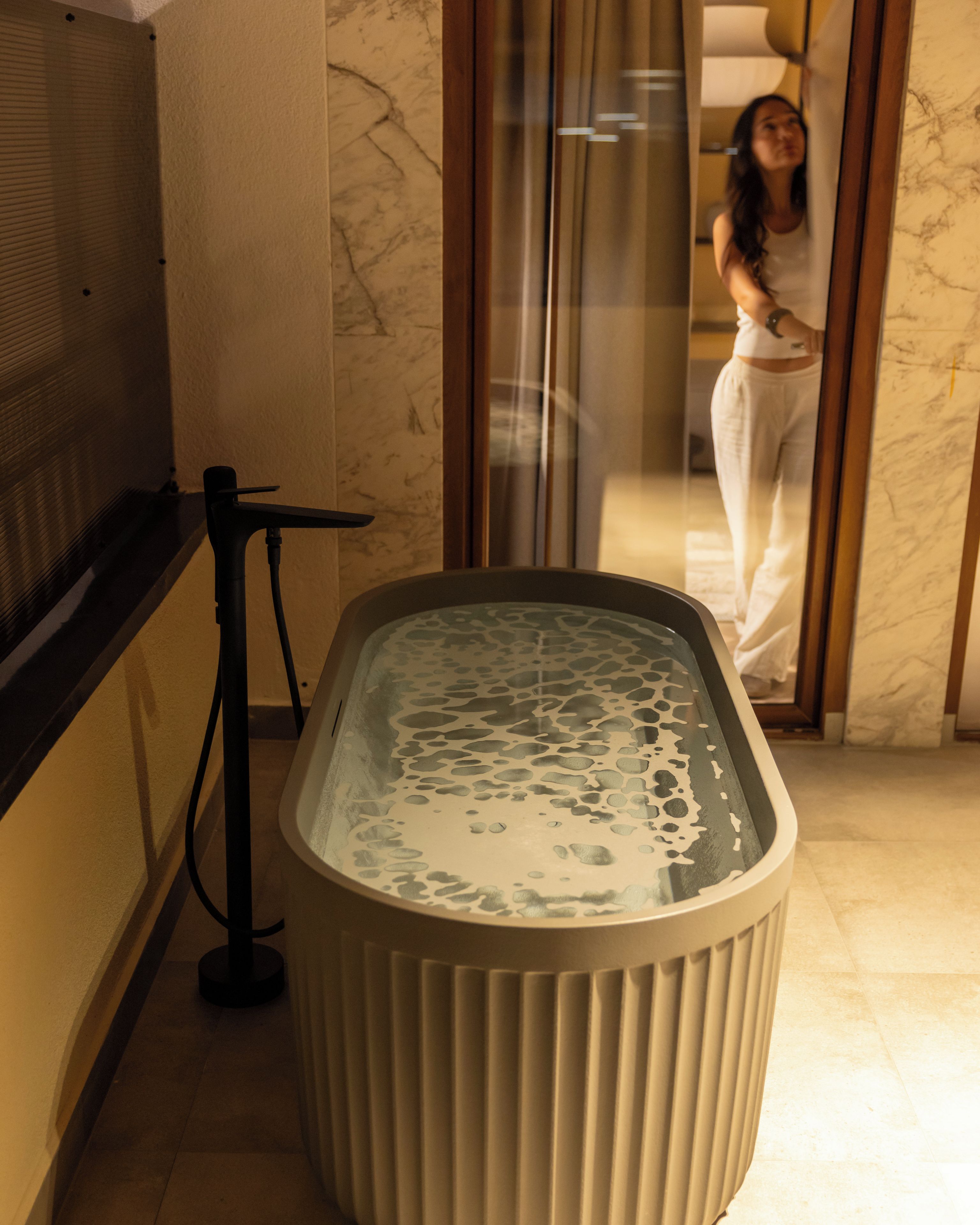 A spa area with a hot tub, a glass door, and a marble wall.