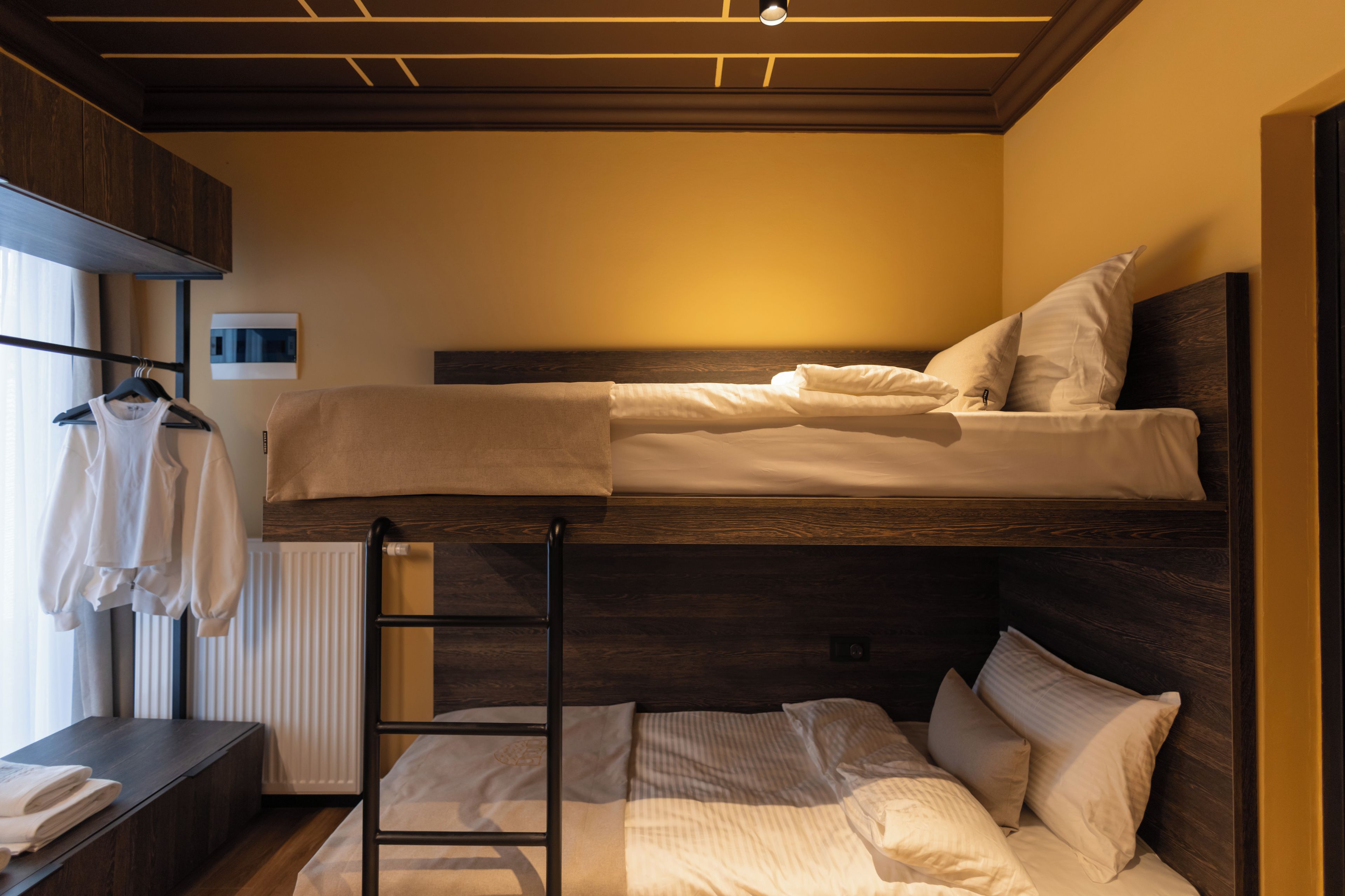 Una cama litera con escalera, una mesita con una toalla y un radiador.
