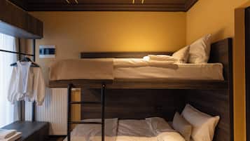 Una cama litera con escalera, una mesita con una toalla y un radiador.