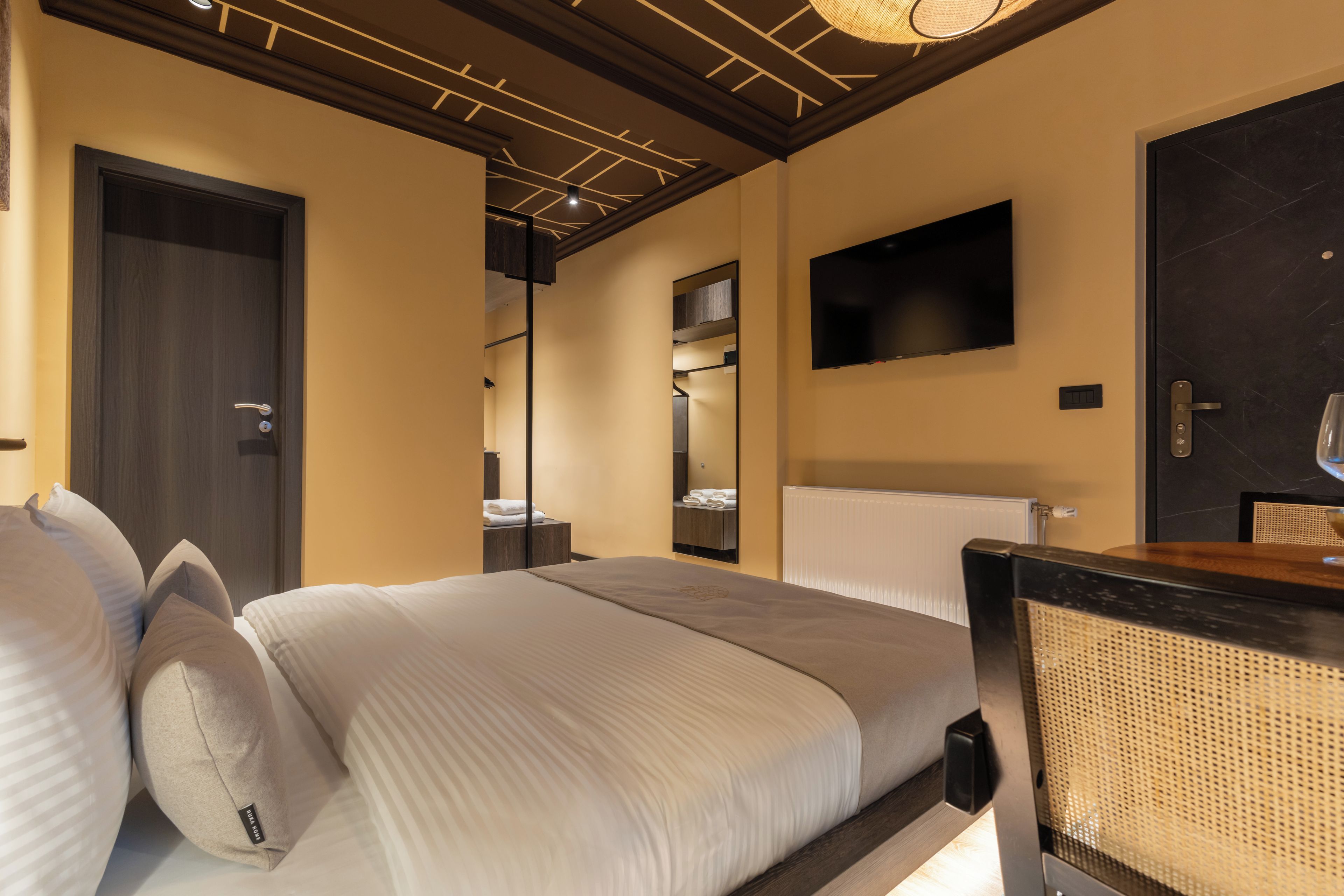 A hotel room with a bed, a flat-screen TV, a door, and a mirror.