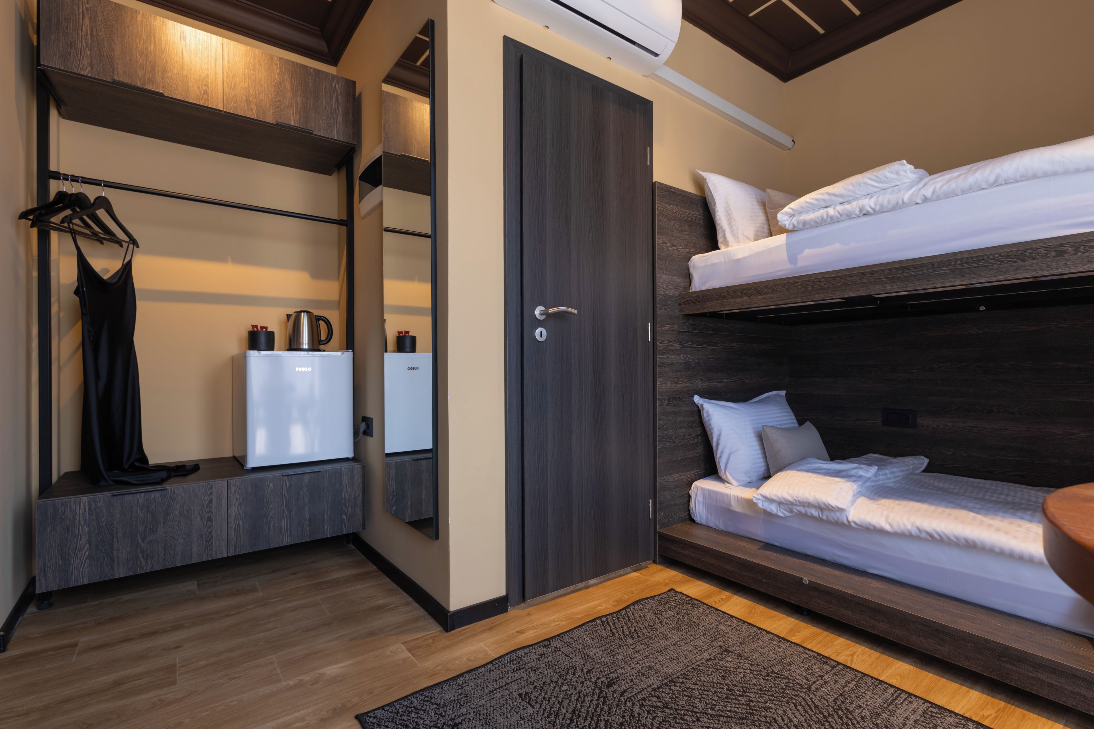 A compact room with a bunk bed, a wardrobe, a mirror, and a small kitchenette.