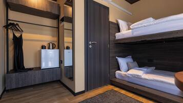 A compact room with a bunk bed, a wardrobe, a mirror, and a small kitchenette.