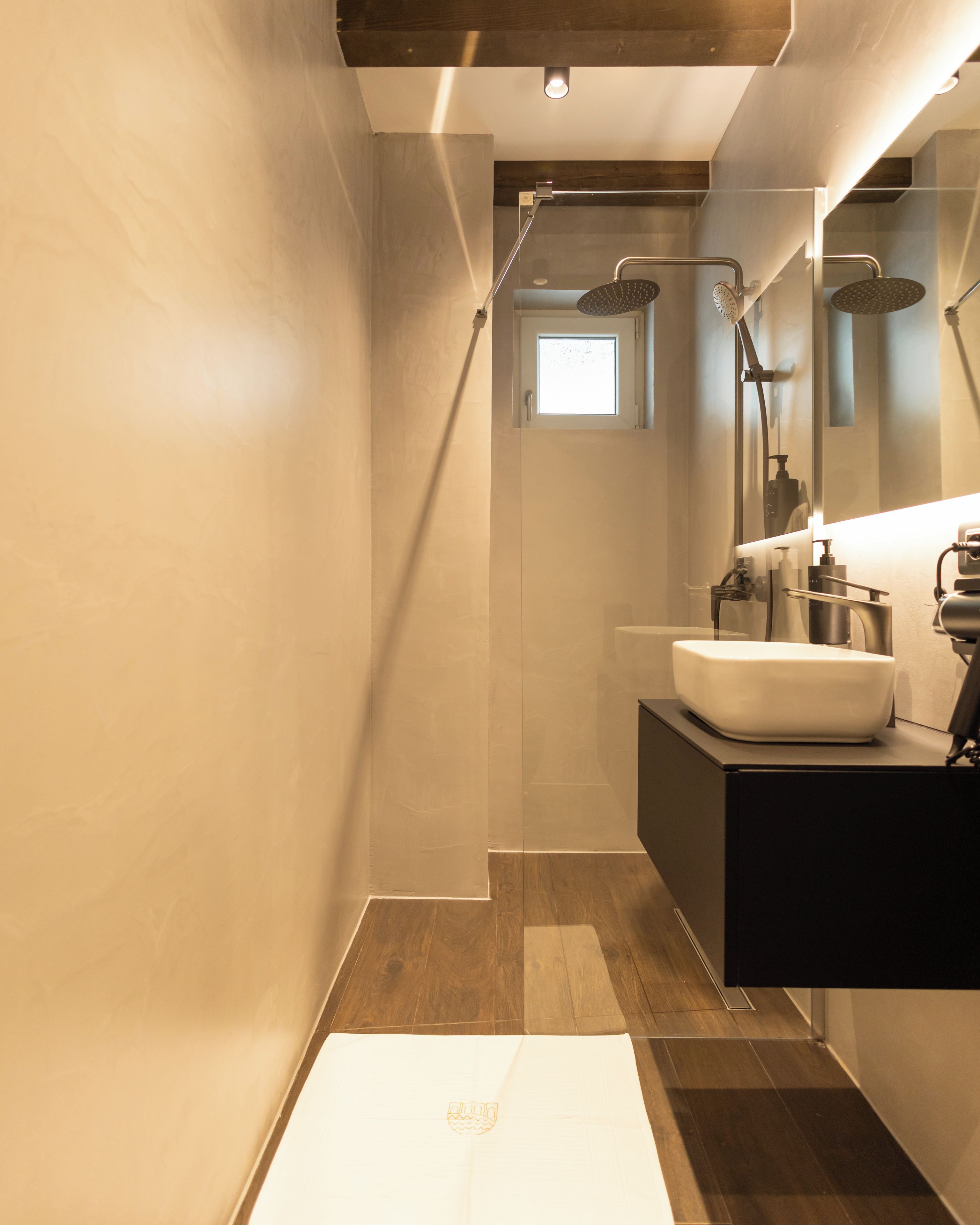 A modern bathroom with a large sink, two showerheads, and a small window.