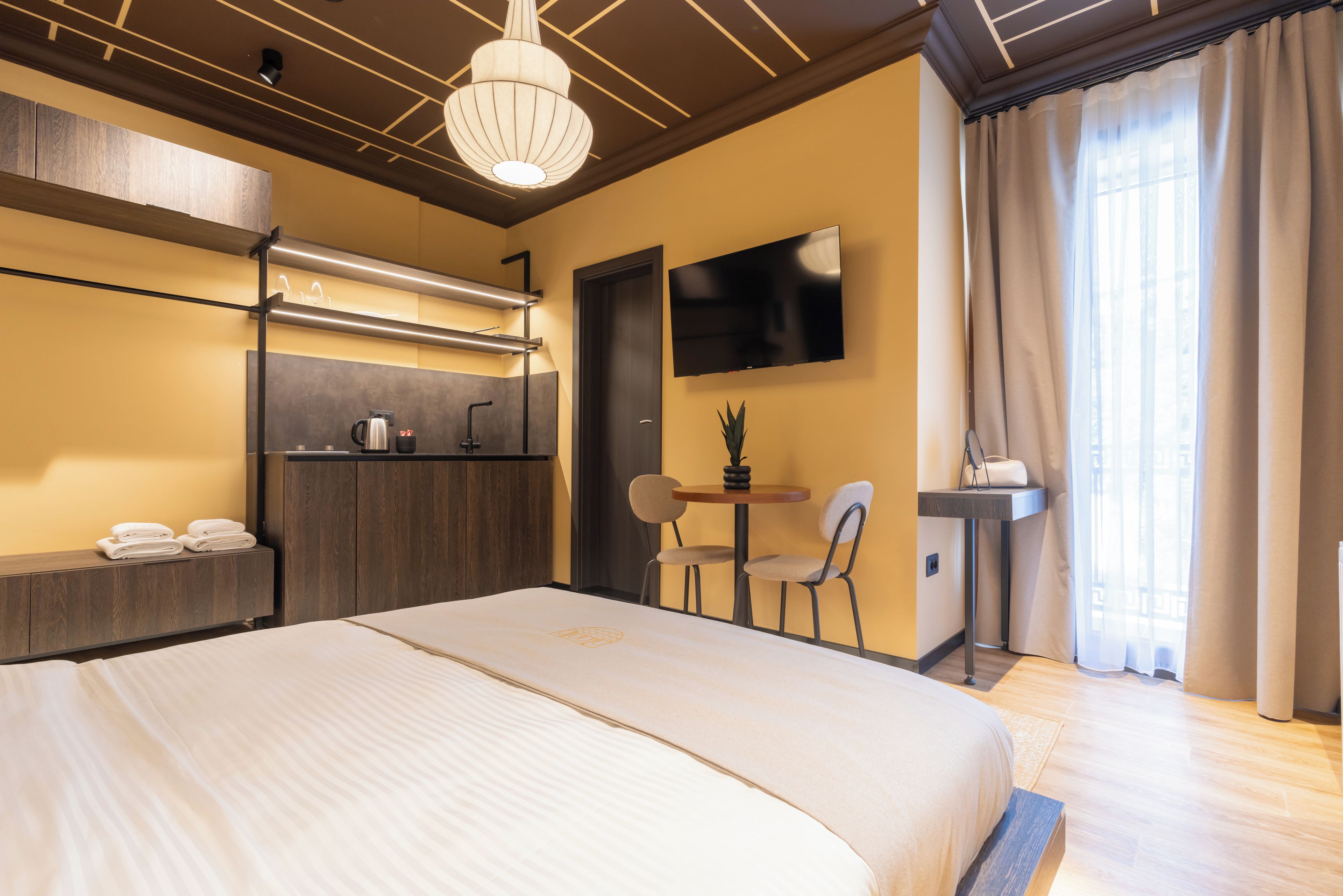 A hotel room with a large bed, a desk with a chair, a TV mounted on the wall, and a window with curtains.
