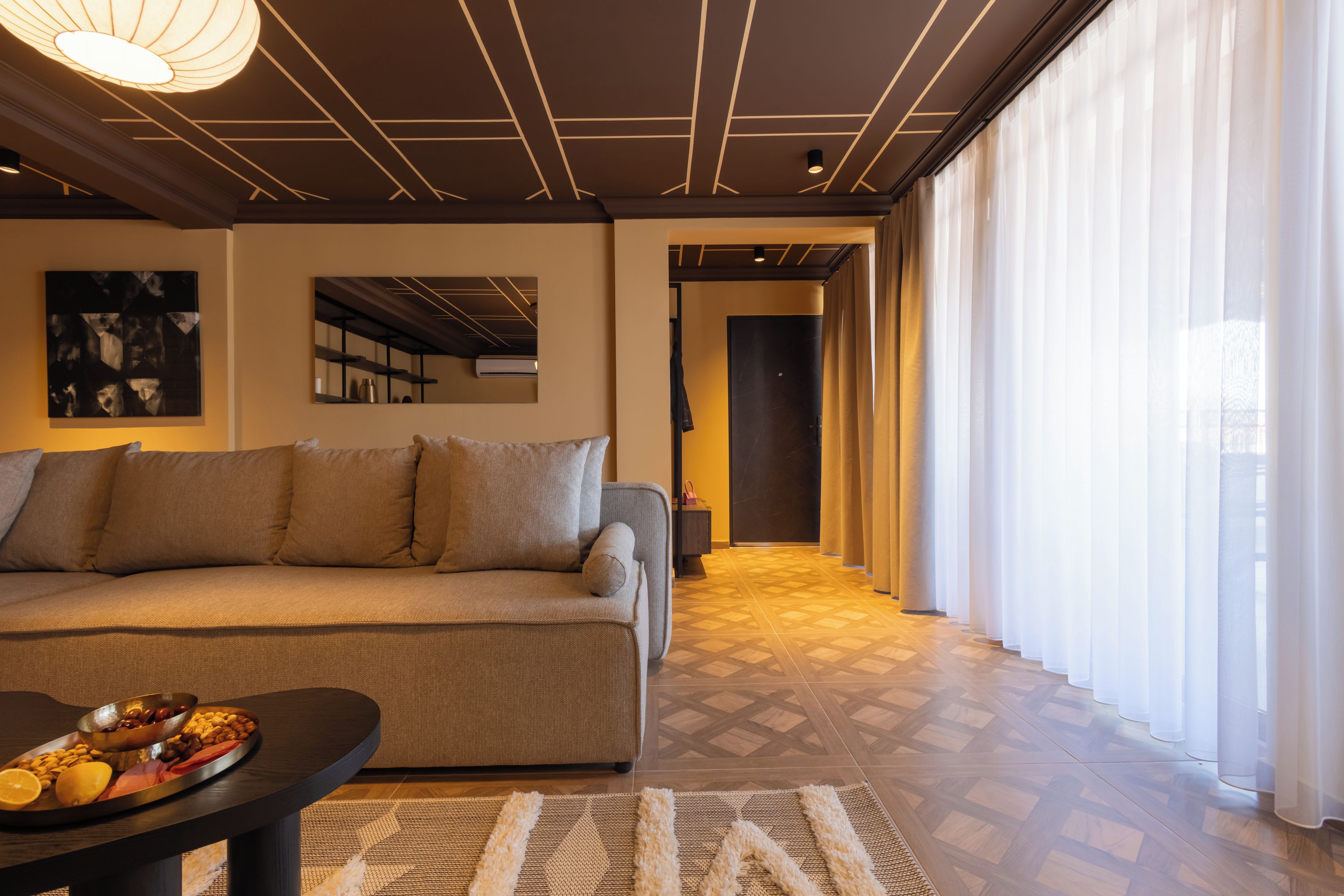 A modern living room with a sofa, a coffee table with snacks, a patterned rug, and a hallway leading to a door.