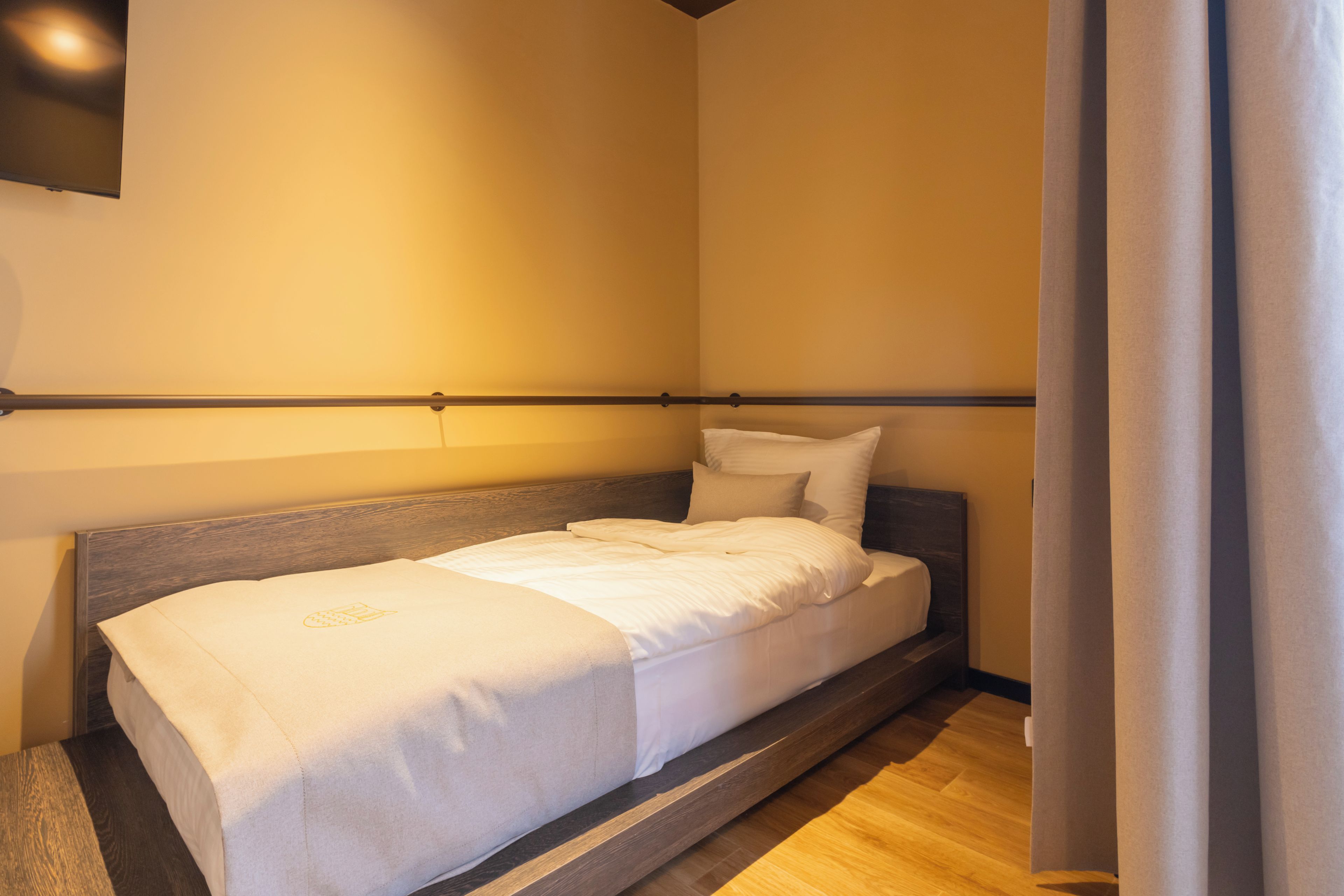 A single bed with a wooden headboard in a room with a wooden floor and a plain wall.