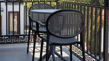 A balcony with a black metal table and two chairs, a decorative black and white railing, and a building in the background.