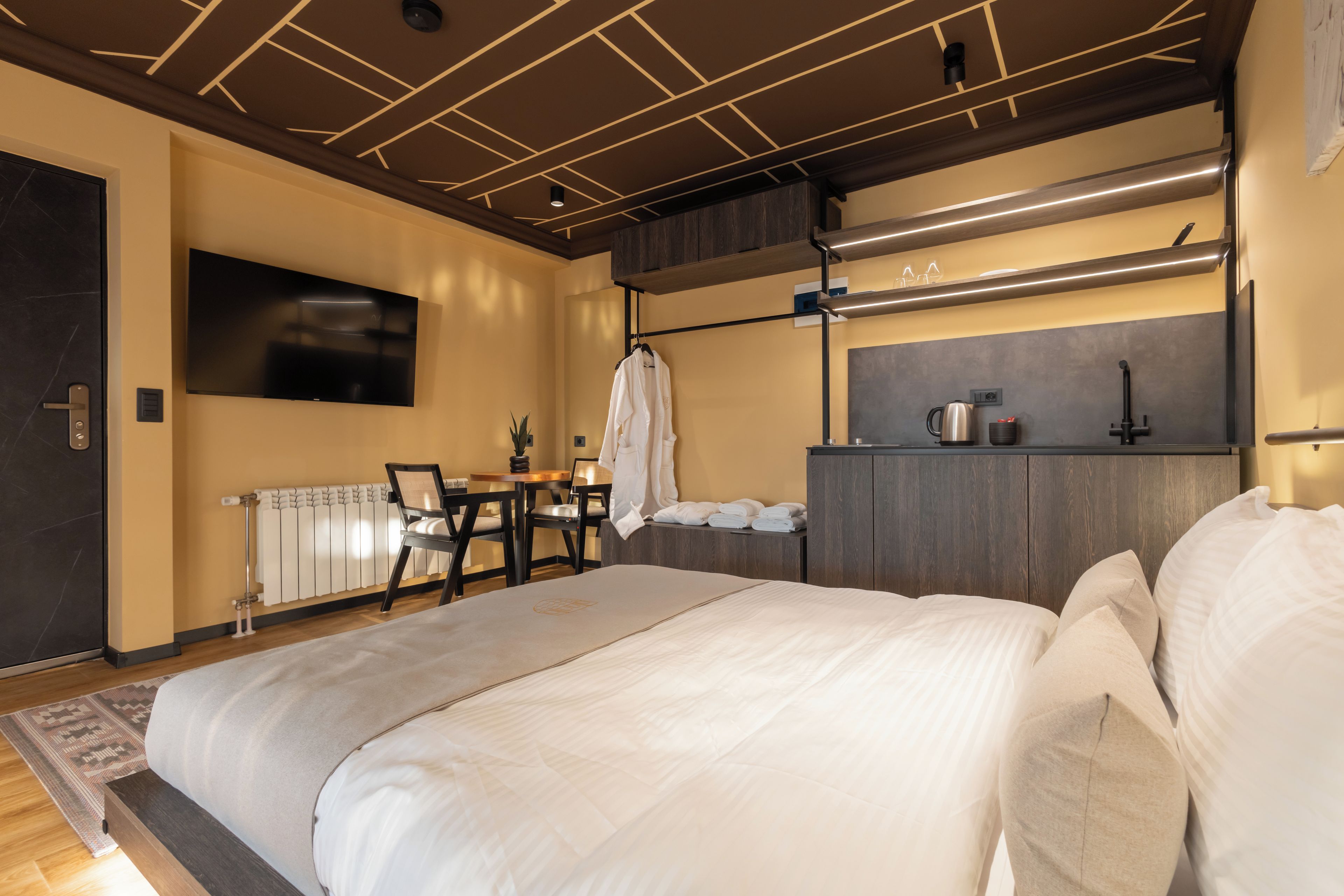 Una habitación de hotel moderna con una cama grande, un escritorio, un televisor de pantalla plana y una kitchenette.