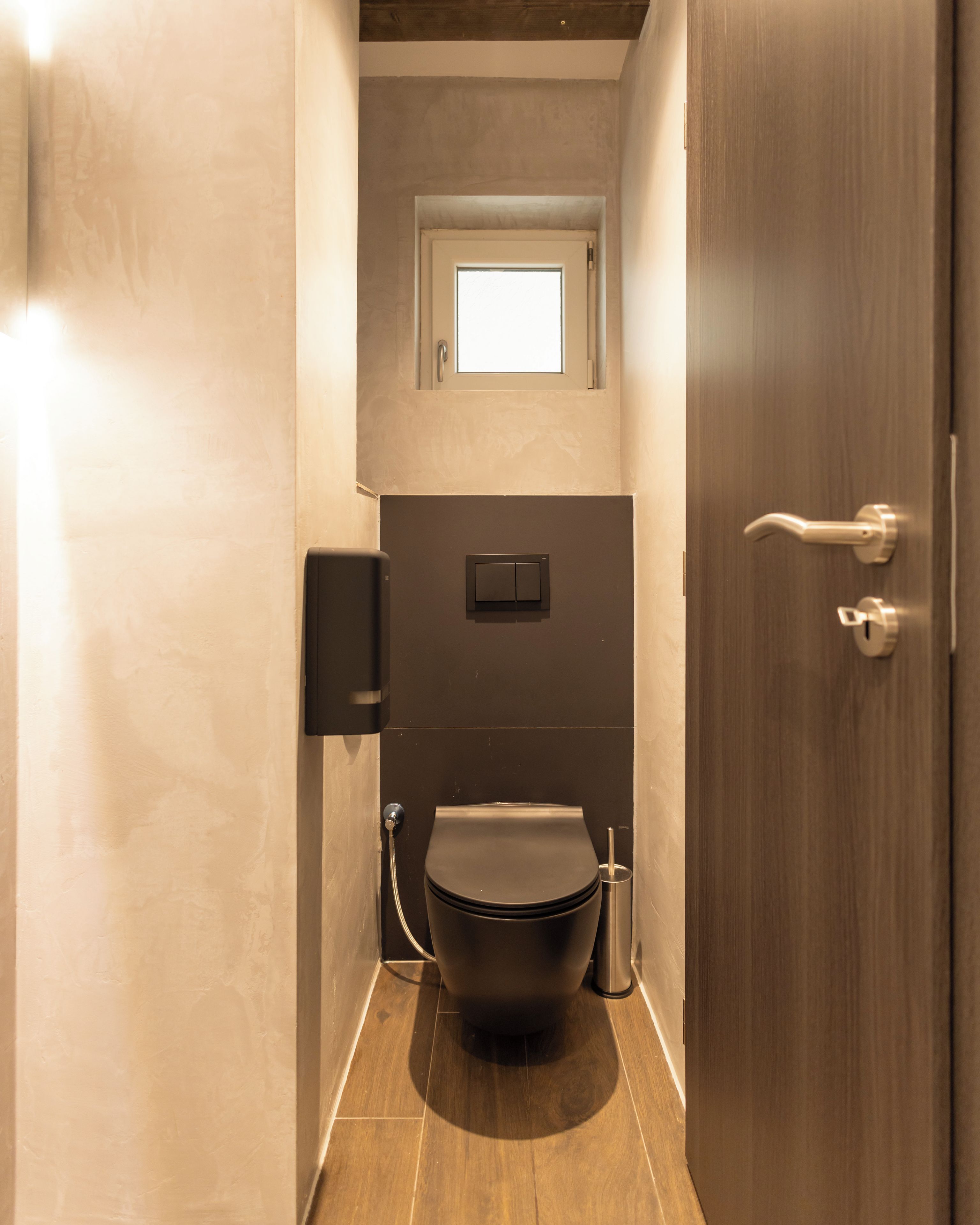 A narrow bathroom with a toilet, a bidet, and a small window above the toilet.