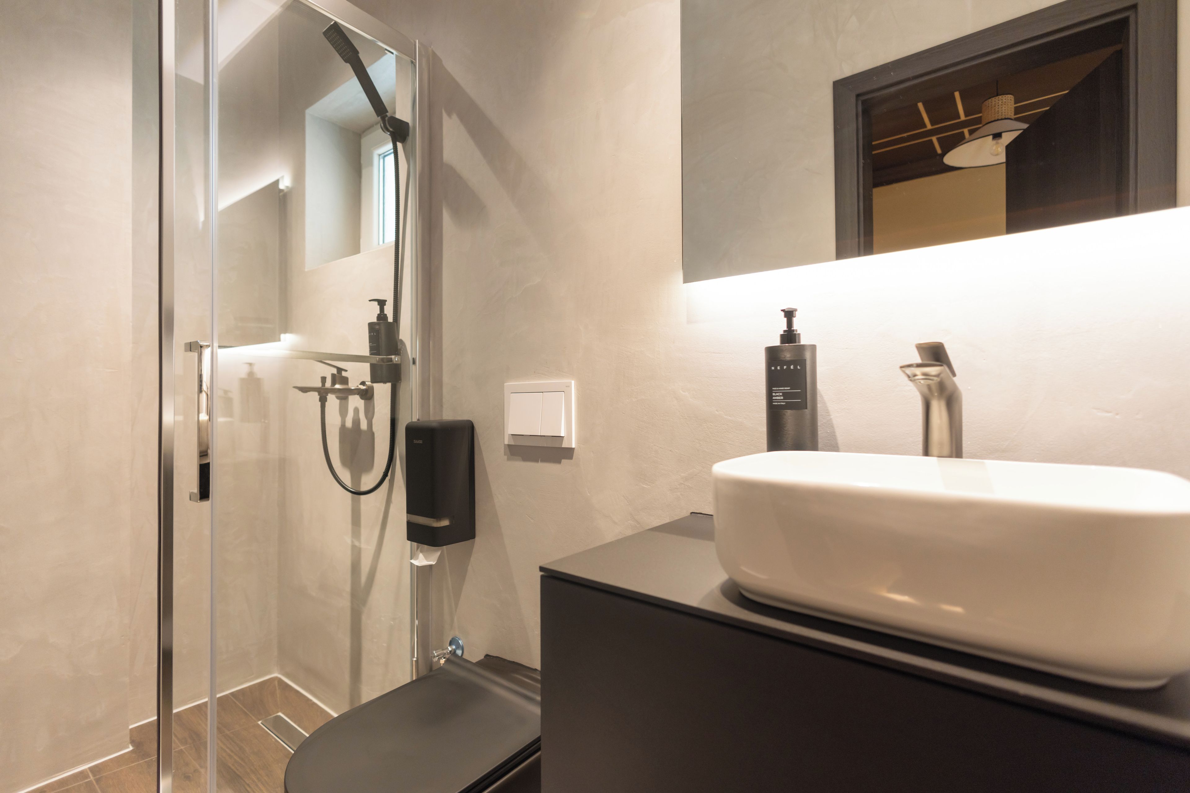 A modern bathroom with a glass shower enclosure, a white sink, and a dark-toned vanity.