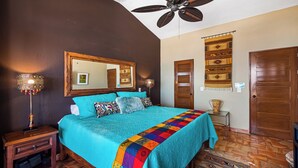 A bedroom with a bed, a ceiling fan, a nightstand, a lamp, a mirror, and a door. - SPECTACULAR views of Banderas Bay One Bedroom Condo in Centro (Puerto Vallarta)