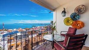 A balcony with a table and chairs, a view of the city, and decorative plates on the wall. - SPECTACULAR views of Banderas Bay One Bedroom Condo in Centro (Puerto Vallarta)