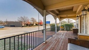 Eine überdachte Veranda mit Geländer, Holzterrasse und Sitzgelegenheit im Freien.