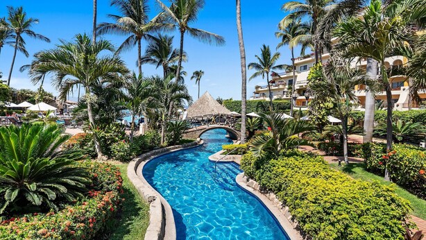 A swimming pool with a bridge, surrounded by palm trees and greenery. - Velas Resort Access Beachfront 3BR Condo (Puerto Vallarta)