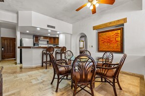 A dining area with a central table and chairs, a ceiling fan, and a kitchen in the background. - Velas Resort Access Beachfront 3BR Condo (Puerto Vallarta)