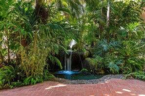 Un jardín con cascada, follaje denso y un sendero de ladrillo.