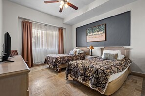 A hotel room with two beds, a desk, a ceiling fan, a window with curtains, and a painting on the wall. - Velas Resort Access Beachfront 3BR Condo (Puerto Vallarta)