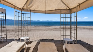 A beach cabana with a view of the sea, two sunbeds, and a small table. - Velas Resort Access Beachfront 3BR Condo (Puerto Vallarta)