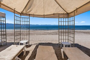 Una cabaña en la playa con vista al mar, dos tumbonas y una mesita.