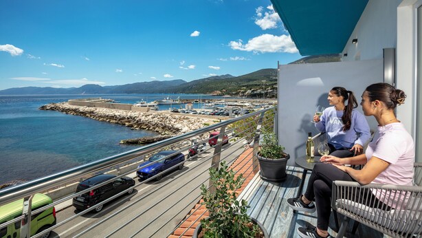 Un balcón con vista al mar, un coche aparcado y una planta en maceta.