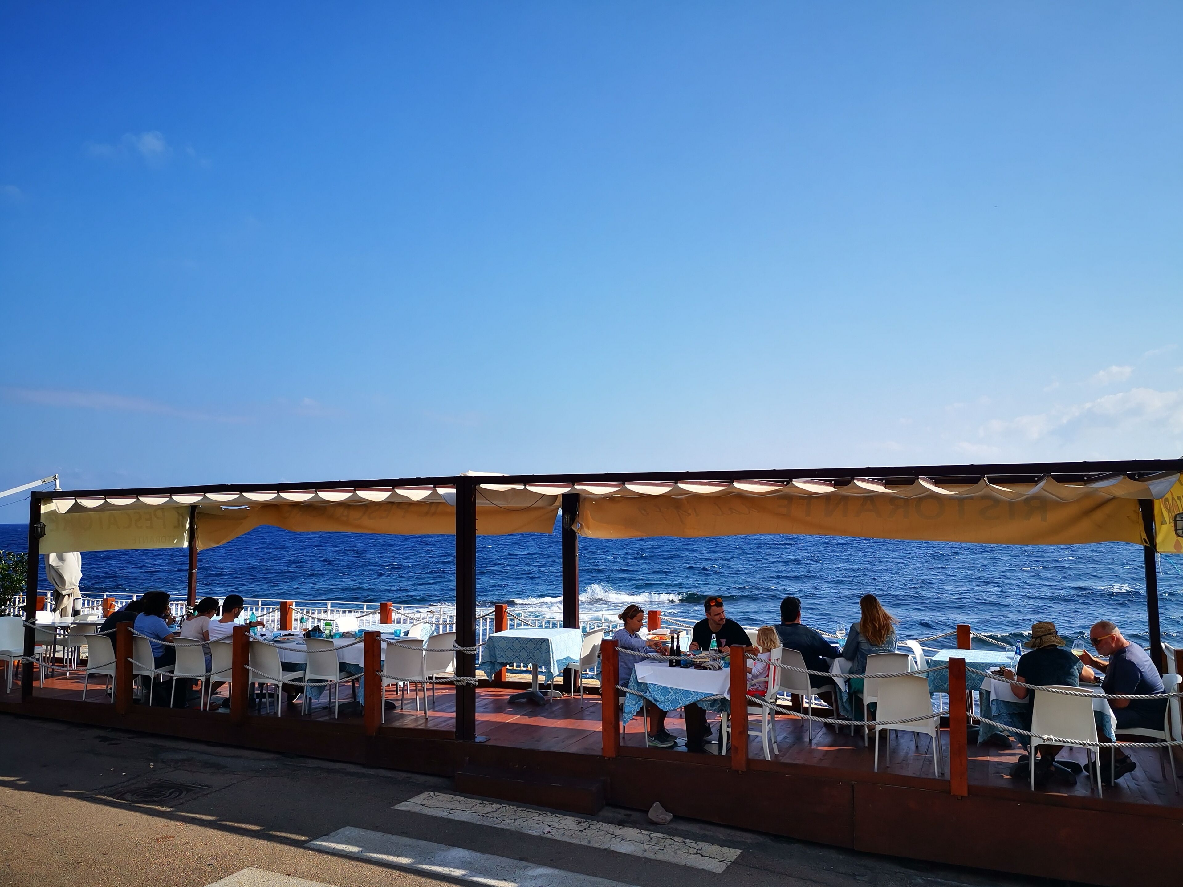Un restaurante frente al mar con terraza, mesas y sillas.