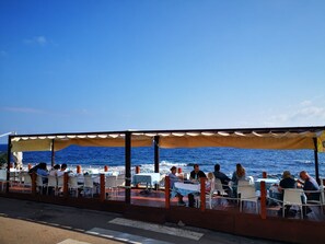 Un restaurante frente al mar con terraza, mesas y sillas.