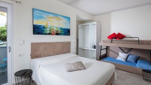 Un dormitorio con una cama grande, una litera, un cuadro de un velero y una mesita pequeña.