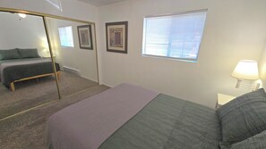 A bedroom with a bed, a mirror, two framed pictures, a window with blinds, and a nightstand with a lamp. - Large Home, Sleeps 13, Hot Tub, Views, Starlink (Eagar)