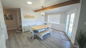 Un comedor con mesa y bancos de madera, una araña y un cuadro en la pared.