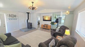 A living room with a fireplace, a sofa, a TV, and a kitchen in the background. - Large Home, Sleeps 13, Hot Tub, Starlink, Air Conditioning (Eagar)