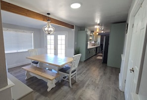 A dining area with a wooden table and benches, a chandelier, and a view of the kitchen.