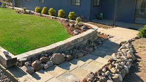 A residential house with a stone retaining wall, a well-maintained lawn, and a driveway leading to the garage. - Large Home, Sleeps 13, Hot Tub, Starlink, Air Conditioning (Eagar)
