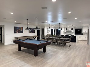 Ein modernes Wohnzimmer mit Billardtisch, Essbereich, Küche und Kunstwerken an den Wänden.