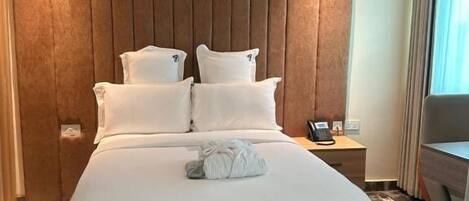 A hotel room with a large bed, a bedside table with a phone, and a desk with a chair.