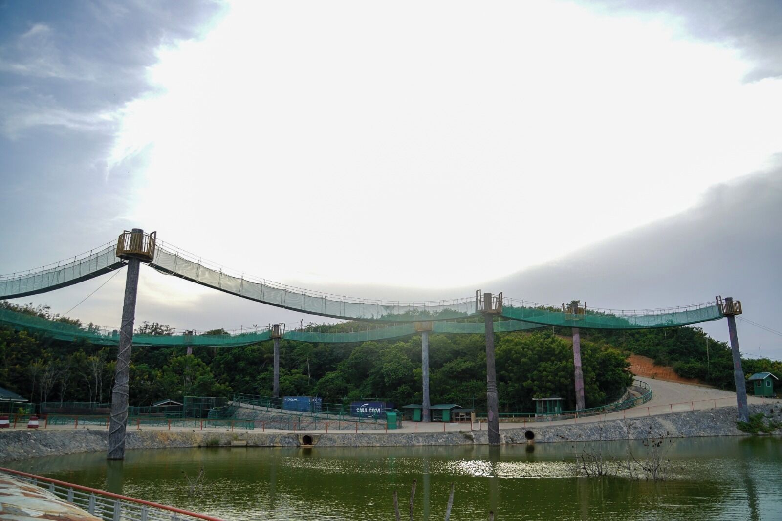 Un pont suspendu enjambant une étendue d’eau, avec une colline boisée en arrière-plan.