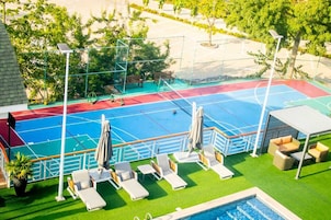 Una cancha de tenis al aire libre con piscina, sillas de descanso y una zona de estar cubierta.