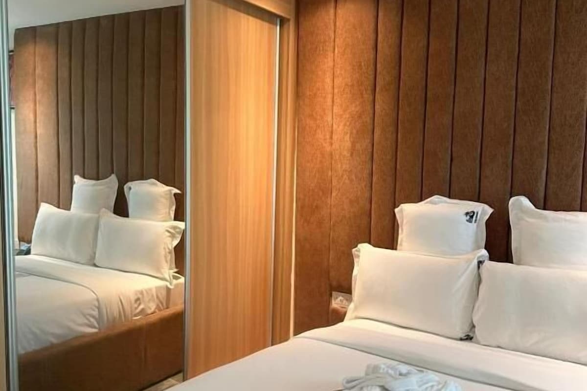 A hotel room with a large bed, a wooden panel wall, and a mirror.